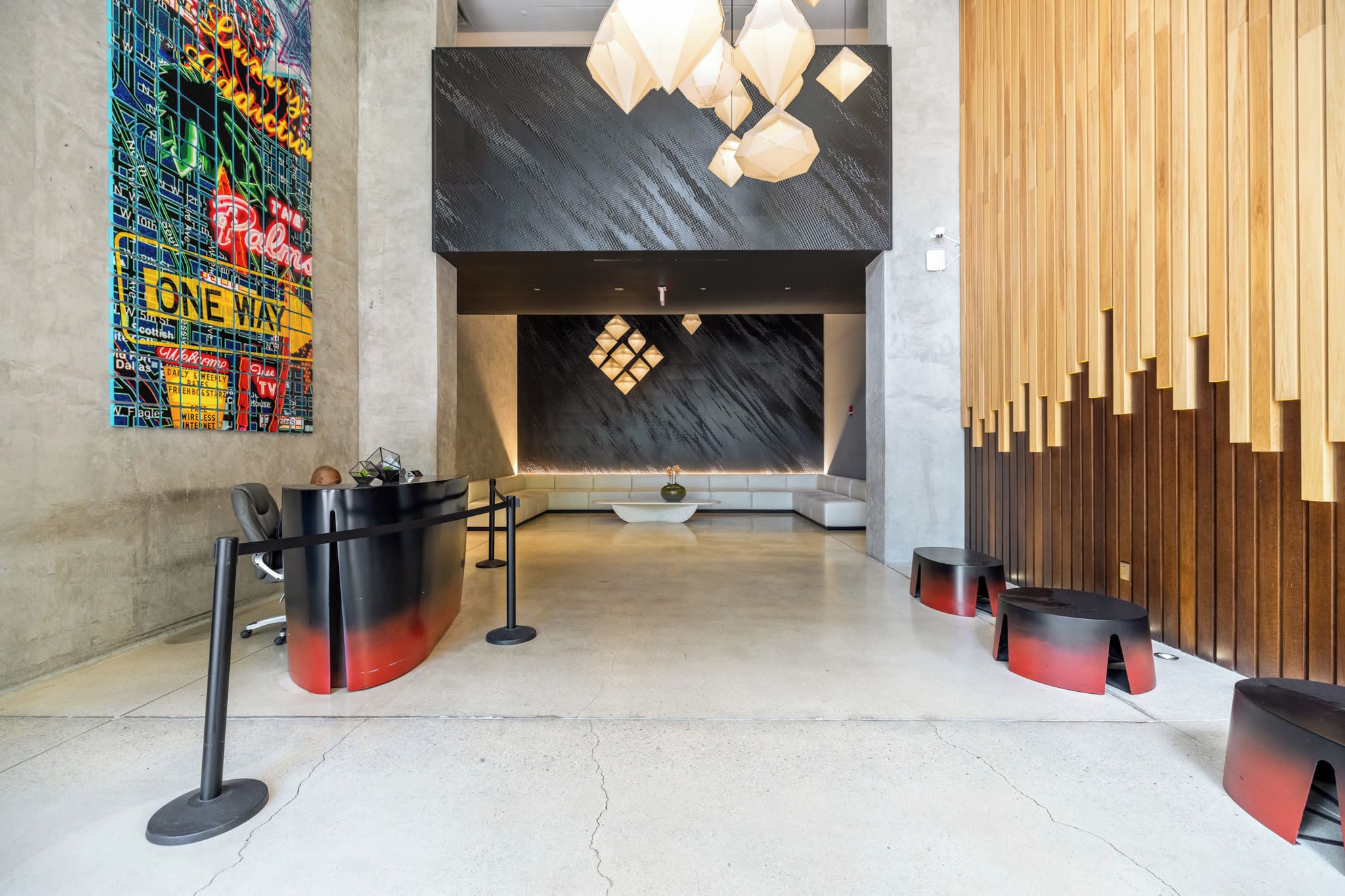 A lobby with a reception desk, a colorful mural, a modern chandelier, and wooden slats on the wall.