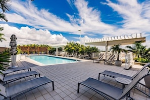 Zona de piscina con sillones de descanso, una pérgola y una valla blanca.