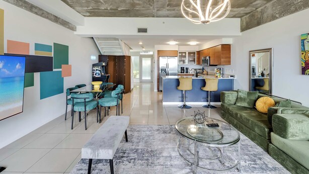Un salon moderne avec une table basse en verre, un canapé et un coin repas avec des chaises de couleur turquoise.