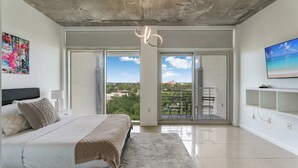 Une chambre moderne avec un lit, une grande fenêtre, un balcon et une vue sur la ville.