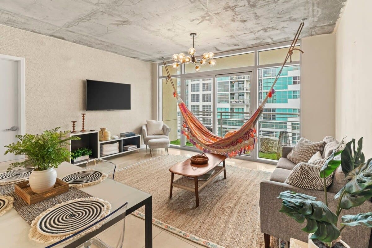 A modern living room with a hammock, a flat-screen TV, a sofa, and a large window with a city view.