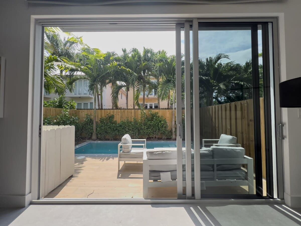 Una habitación con puerta corrediza de vidrio que da a una zona de piscina con mobiliario exterior.