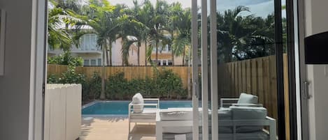 Una habitación con puerta corrediza de vidrio que da a una zona de piscina con mobiliario exterior.