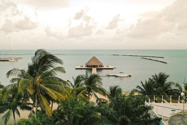 A tropical resort with a thatched-roof structure on a pier, surrounded by palm trees and calm sea.