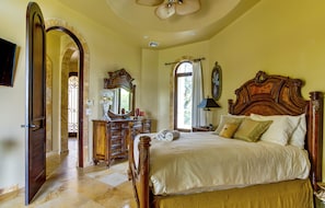 A spacious bedroom with a large bed, a wooden dresser, a vanity with a mirror, and a door leading to another room. - Villa Castello, Private, Amenities, Walk to Beach (Placencia)