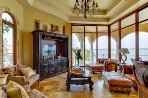 A spacious living room with a fireplace, comfortable seating, and large windows offering a view of the sea.
