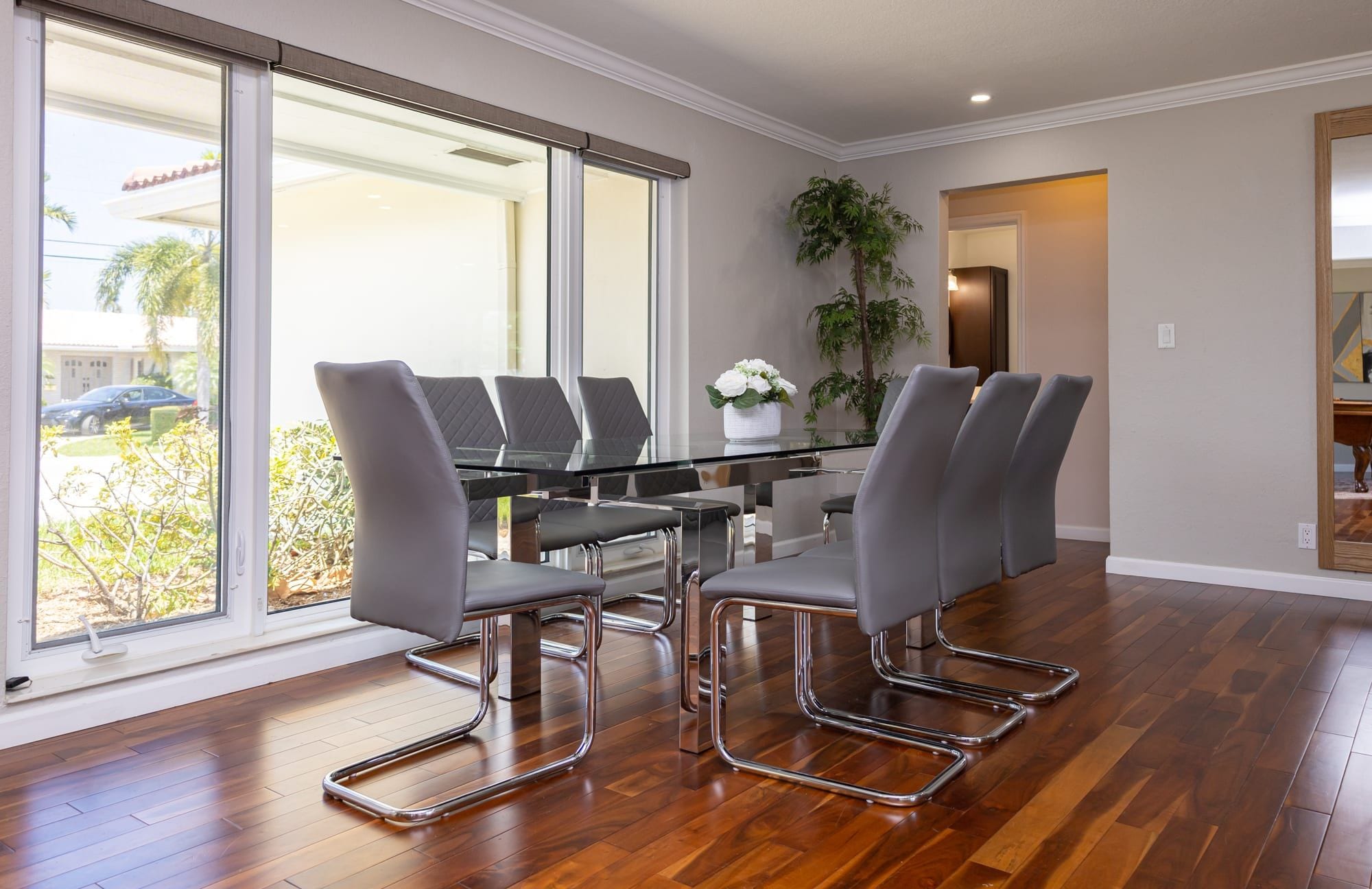 A modern dining area with a glass table, metal chairs, and a view through large windows.