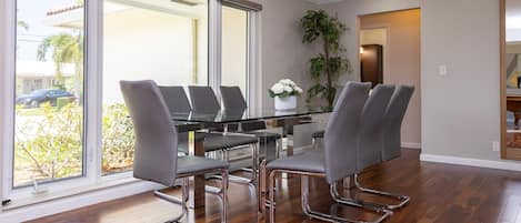 A modern dining area with a glass table, metal chairs, and a view through large windows.