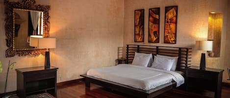 A bedroom with a large bed, two bedside tables, a mirror, and three wall-mounted paintings.