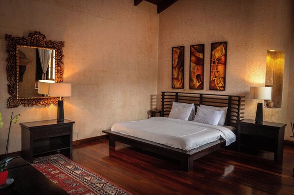 Een slaapkamer met een groot bed, twee nachtkastjes, een spiegel en drie aan de muur hangende schilderijen.
