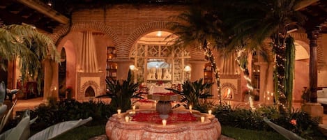 A courtyard with a central fountain, palm trees, and a building with arches and columns.