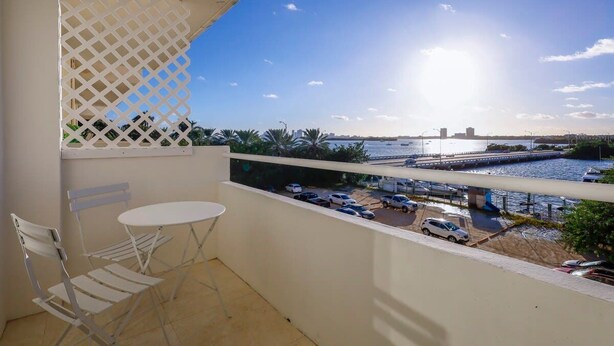A balcony with a white table and chairs, overlooking a marina with boats and a bridge. - La Marinita, Quaint, Water Views Minutes to Beach (North Bay Village)