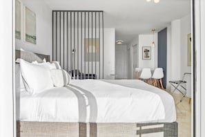 Une chambre d’hôtel moderne, dotée d’un grand lit, d’un bureau, de deux chaises et offrant une vue sur la ville par la fenêtre.