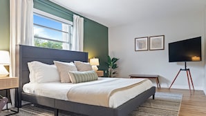 Un dormitorio moderno con una cama grande, televisión y ventana con cortinas.