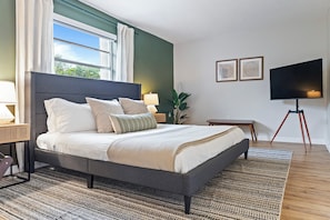Un dormitorio moderno con una cama grande, televisión y ventana con cortinas.