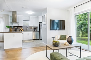 Una cocina moderna con gabinetes blancos, electrodomésticos de acero inoxidable y un comedor con mesa y sillas verdes.