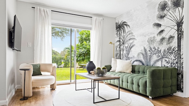 Una sala de estar moderna con un sofá verde, una mesa de centro redonda y vistas a un jardín a través de amplios ventanales.