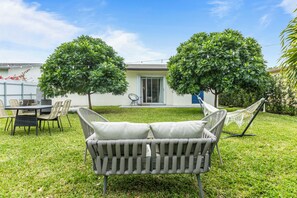A patio with a wicker chair, a dining table with chairs, and two trees.