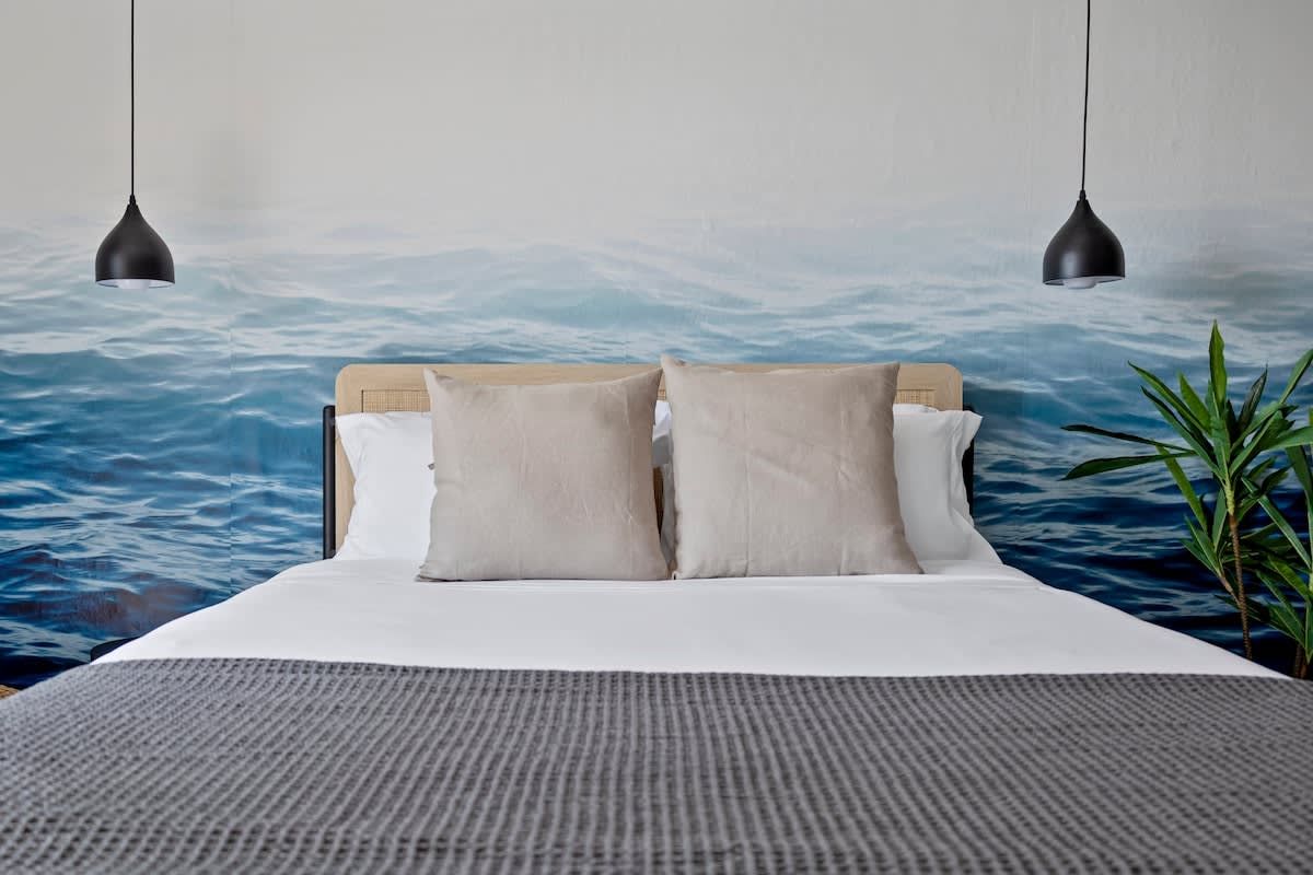 Un letto con testiera, due cuscini, una coperta grigia e materassa, e un affresco a tema acquatico.