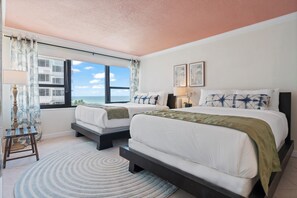 A hotel room with two beds, a view of the sea, a circular rug, and a window with curtains. - Coastal Dreams, Serene, Beachfront With Pool (Miami Beach)