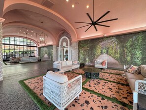 A spacious lobby with a high ceiling, a large arched window, and a mural of a forest pathway. - Coastal Dreams, Serene, Beachfront With Pool (Miami Beach)