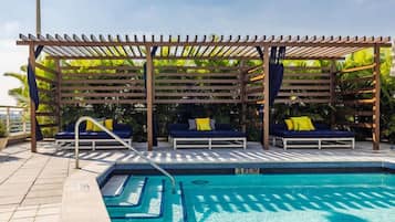 Un área de piscina con una pérgola de madera, sillas de descanso y una piscina azul cristalina.