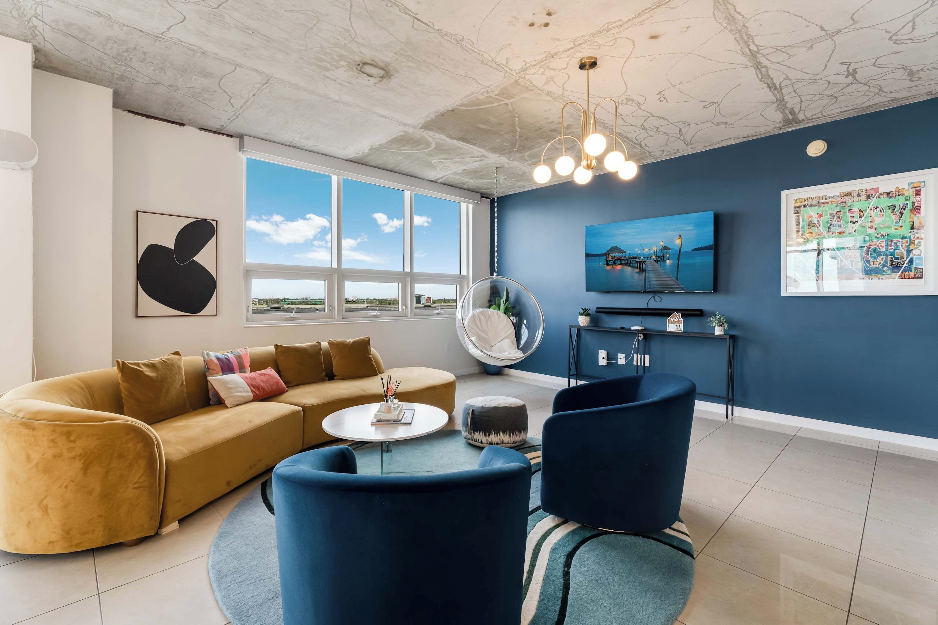 Una sala de estar con sofá, sillas, una mesa de centro, un sillón colgante, televisor y obras de arte en la pared.