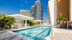A swimming pool with a sunshade, palm trees, and high-rise buildings in the background. - Miami Vice, Chic, Pool and Steps to Midtown Shops (Miami)
