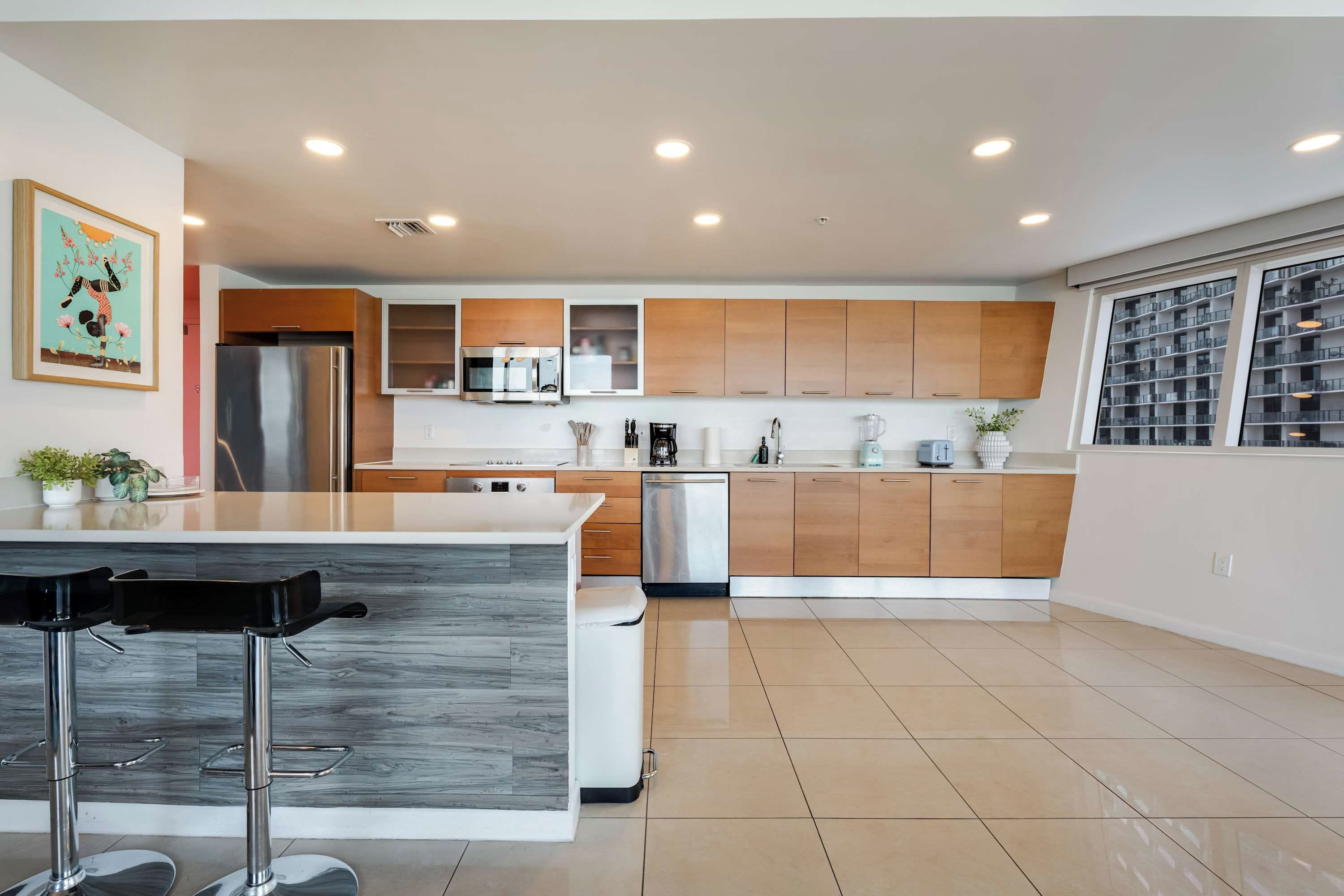Cozinha moderna com ilha central, eletrodomésticos de aço inoxidável, armários de madeira e uma janela grande.
