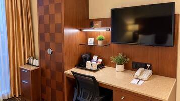 Habitación de hotel con escritorio, televisor de pantalla plana, teléfono, cafetera, planta y minibar.