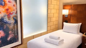 A hotel room with a bed, a nightstand, a wall-mounted lamp, and a painting.