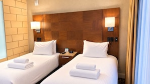 A hotel room with two beds, each with white linens and towels, a wooden headboard, bedside lamps, and a small bedside table with a phone and a clock. - HarbourtFront Center (Toronto)