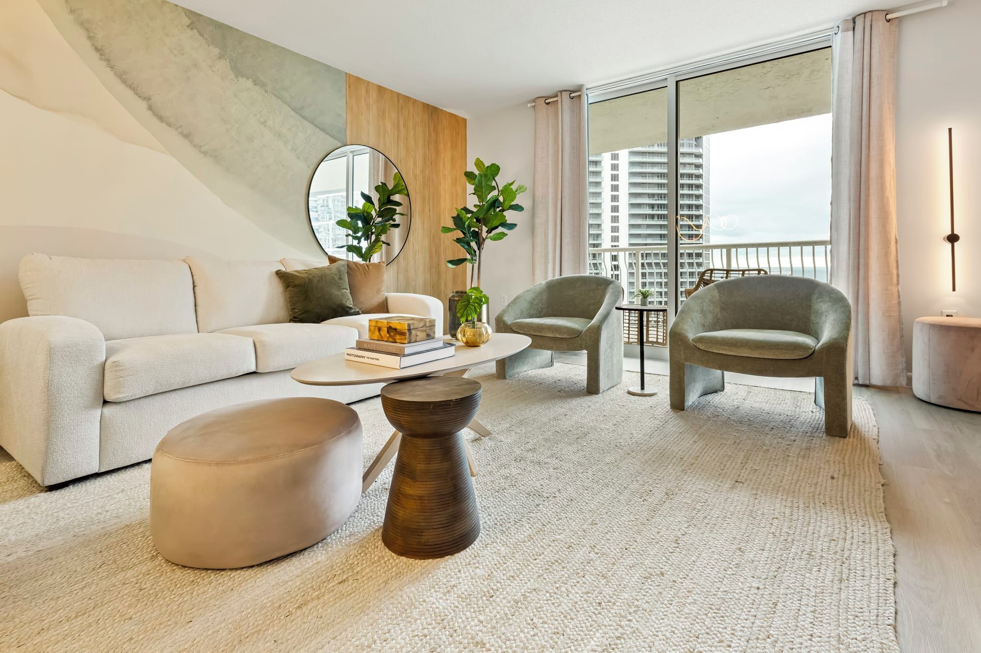 A modern living room with a sofa, two armchairs, a coffee table, and a large window with a view of high-rise buildings.