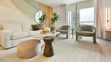 A modern living room with a sofa, two armchairs, a coffee table, and a large window with a view of high-rise buildings.
