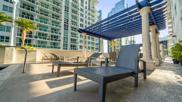 An outdoor seating area with a pergola, lounge chairs, and a column.