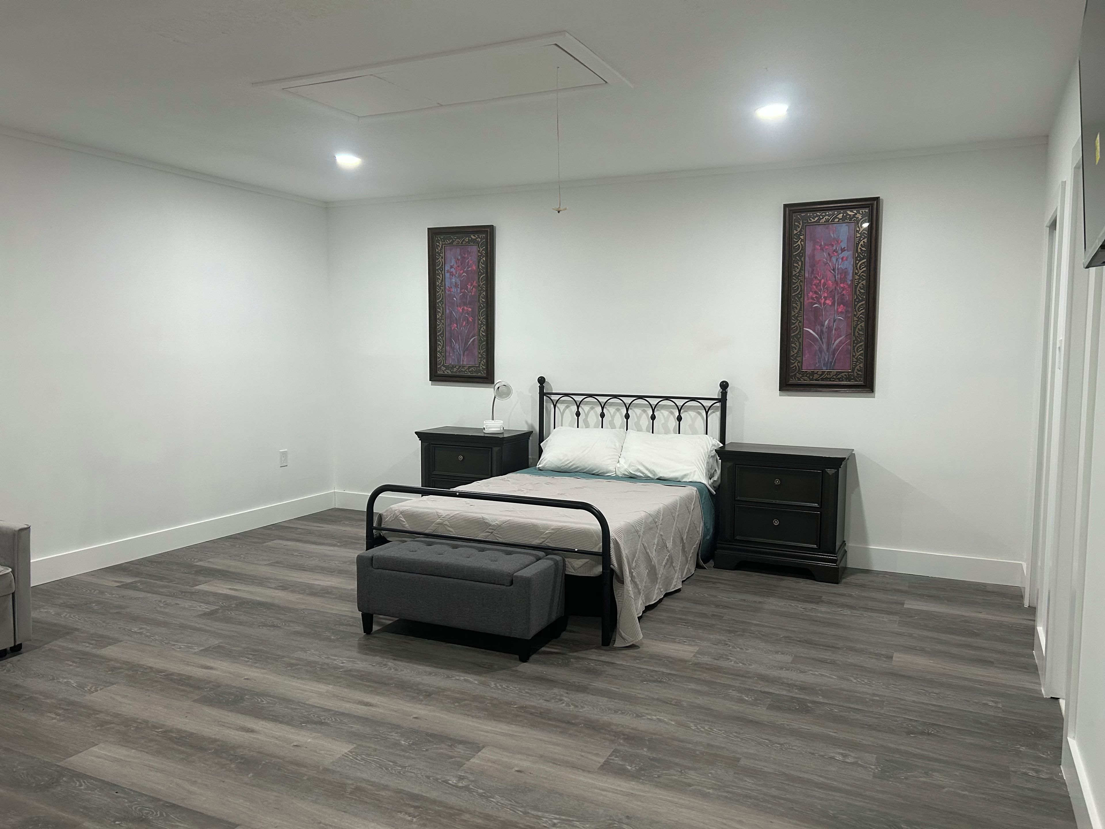 A bedroom with a bed, nightstands, a bench, and two wall-mounted paintings.
