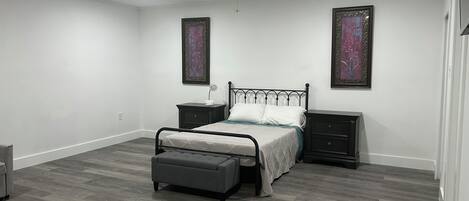 A bedroom with a bed, nightstands, a bench, and two wall-mounted paintings.