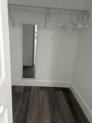 Ein Zimmer mit Holzboden, einer weißen Tür und einem Kleiderschrank mit Kleidung.