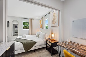A modern hotel room with a bed, bedside table, lamp, and a view of greenery outside. - Casa Ana, Homey Design, Hot Tub in North Miami (Miami Shores)