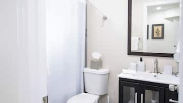 Un baño con inodoro, cortina de ducha, lavamanos con espejo y un cubo de basura.