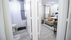 A modern bathroom with a toilet, shower, and a white door leading to a bedroom with a bed and a desk. - Good Vibes Oasis, 2 Story Townhome in Cutler Bay (Cutler Bay)