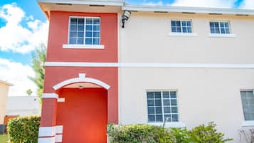 Un edificio de dos pisos con fachada roja y color crema, una entrada visible con un arco blanco y ventanas con marcos blancos.