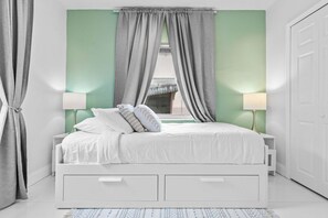 A neatly arranged bedroom with a bed, bedside lamps, and a window with curtains.