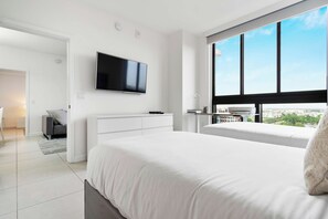 Quarto moderno com uma cama grande, uma TV fixada na parede e vista para a cidade através de amplas janelas.