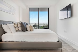 Quarto moderno com uma cama grande, televisão montada na parede e varanda com vista para a cidade.