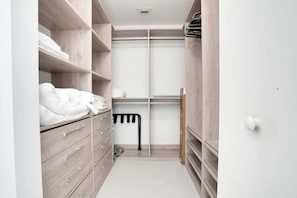 A walk-in closet with wooden shelving, a hanging rack, and a mirrored closet door. - Miami Paraiso, Modern Rooftop Pool Walk to Midtown (Miami)