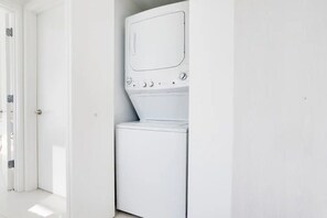 A laundry room with a washer and dryer, a door, and a white wall. - Miami Paraiso, Modern Rooftop Pool Walk to Midtown (Miami)