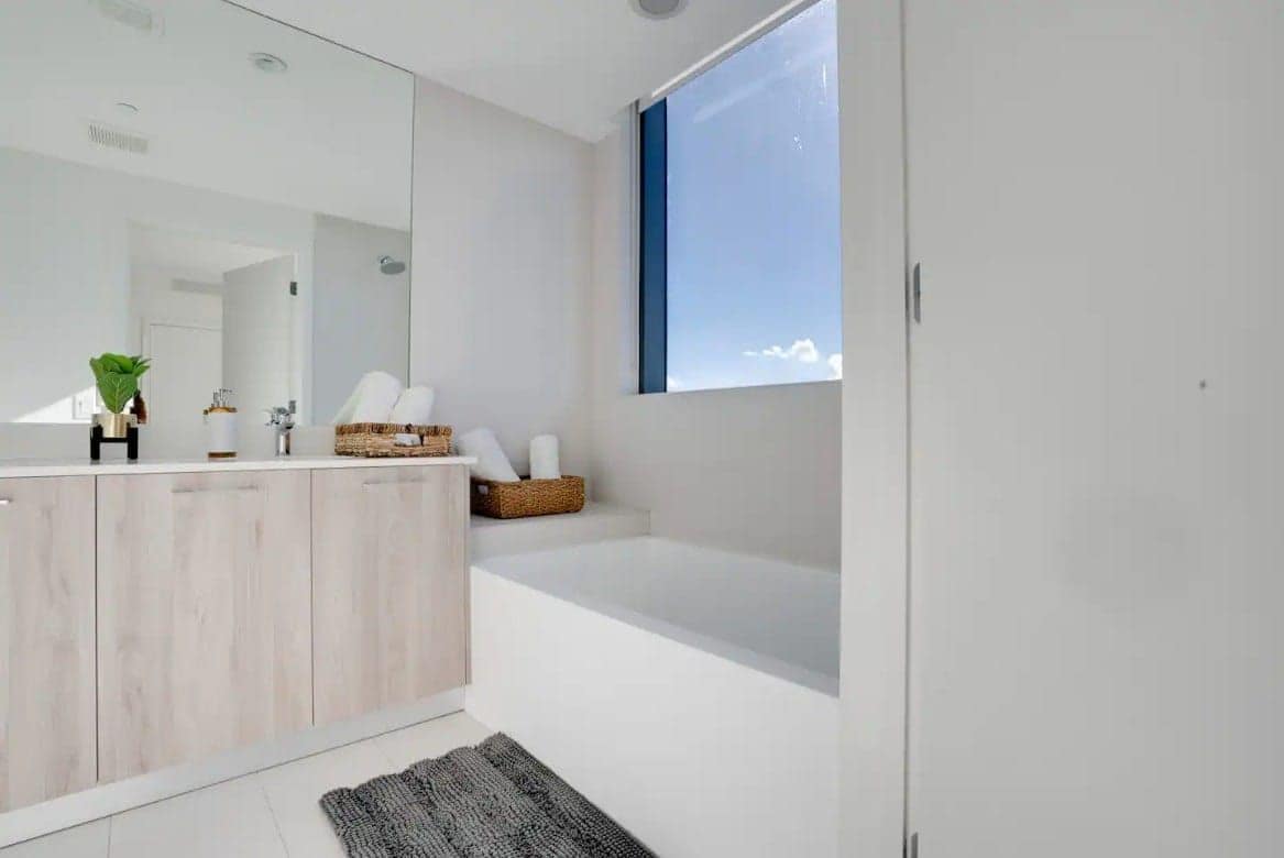 Ein modernes Badezimmer mit einem großen Spiegel, einer Badewanne und einem Fenster.