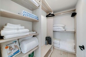 Ein ordentlich eingerichteter Kleiderschrank mit Regalen, auf denen gefaltete Handtücher und eine Matratzenschutzkiste liegen.