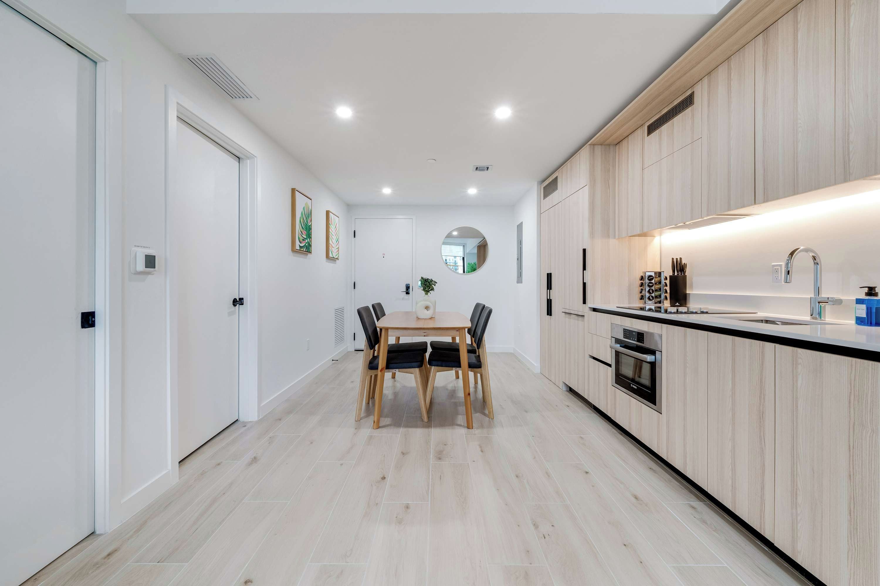 A modern kitchen with wooden cabinets, a central island, and a dining area with a table and chairs.